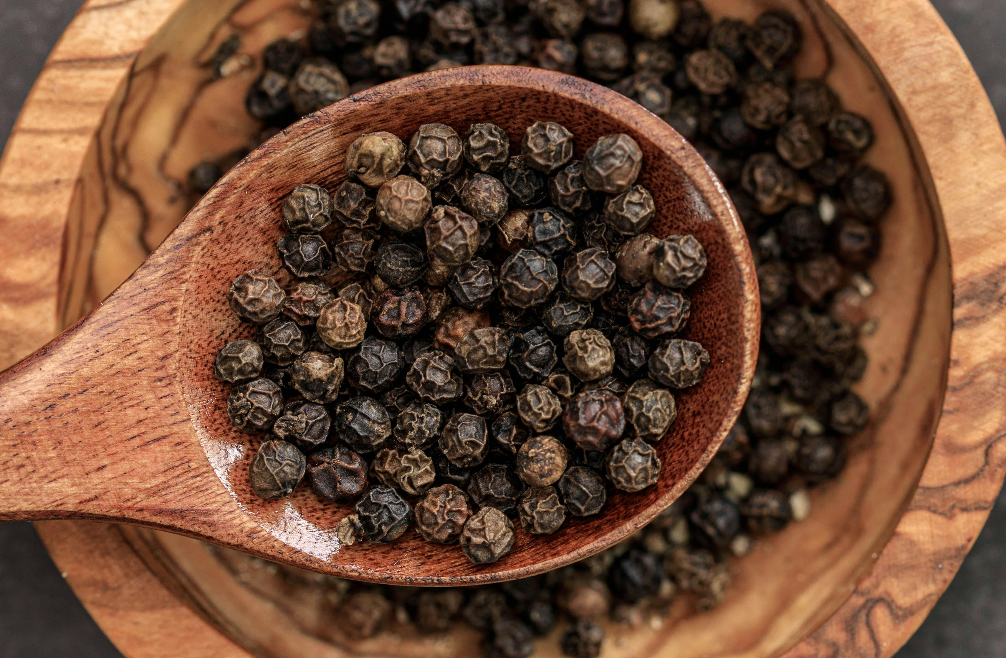 Dried black peppercorns in a wooden spoon